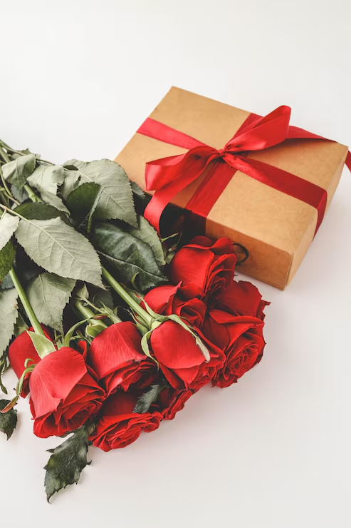 Hand-tied red roses beside a ribboned gift box